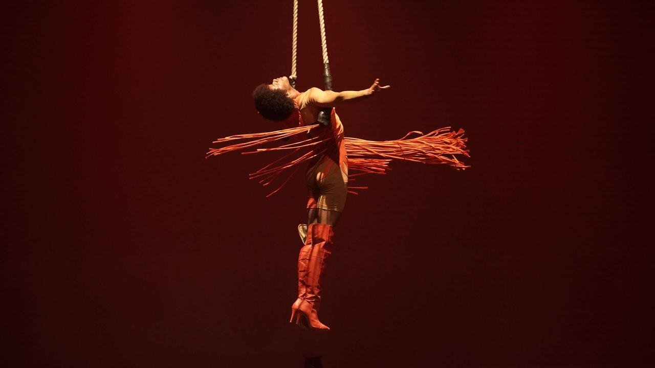 Artista circense se apresentando no tecido aéreo sob luz vermelha